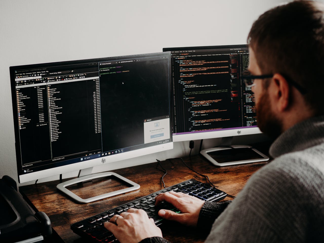 product-04 Software developer typing code on dual monitors at a wooden desk.